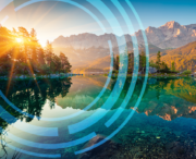 Mountain lake landscape at sunrise with trees and mountains reflected in the water, overlaid with semi-transparent blue circular graphic elements.